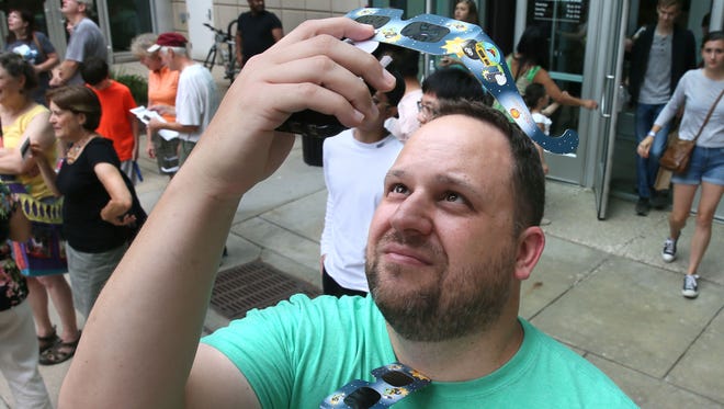 Andrew Nielsen of Wauwatosa put his eclipse glasses over the camera lens in his phone as he tries to take photos of the eclipse.