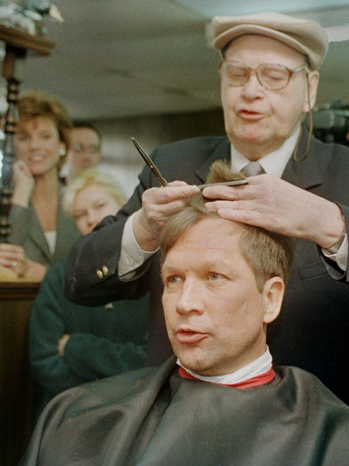 As his wife, Karen, left, watches, Kasich stops in for a haircut by Joe Swiezynski in Milford, N.H., on Feb. 15, 1999, during a campaign swing.
