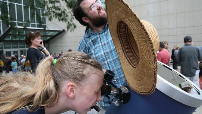 Ariella Beyerlein, 12, of Mukwonago looks through one of the telescopes at the event as Graham Rhoads of Random Lake shields her eyes with his hat.