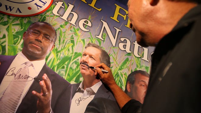 Kasich draws a mustache on a picture of himself at the Republican Party of Iowa booth at the Iowa State Fair on Aug. 18, 2015, in Des Moines.