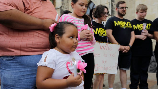 Mia Gonzalez holds a flower and artificial candle as she takes part in a vigil at San Fernando Cathedral for victims who died as a result of being transported in a tractor-trailer, July 23, 2017, in San Antonio.