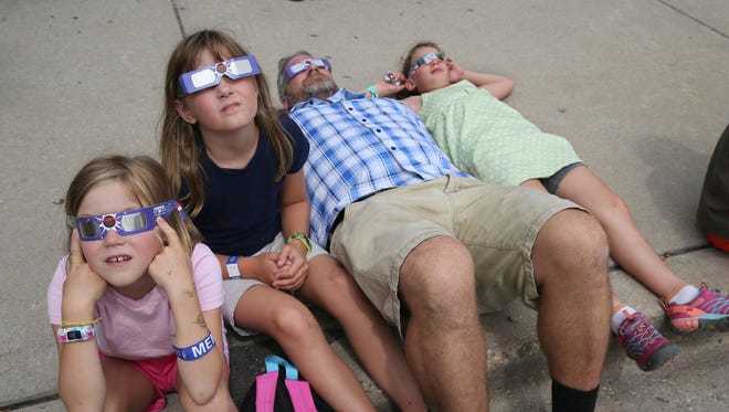 (From left) Lilly Apitz, 8, her twin sister Daphne Apitz, 8, their father Branden Apitz, all of Milwaukee, and Maya Lemery, 4, of Grand Chute lay back on the sidewalk to watch the eclipse.